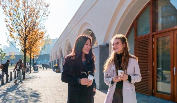 Twee studenten lopen lachend met een kopje koffie op straat in Rotterdam