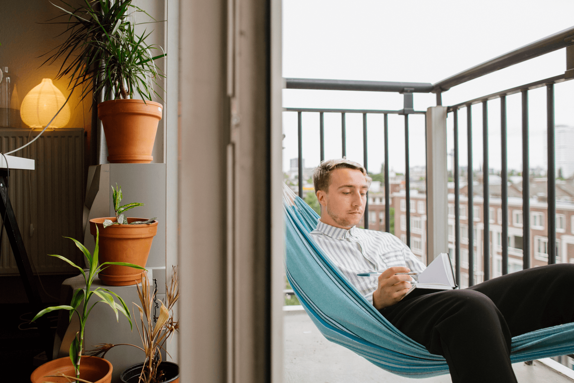 Student in Rotterdam ligt in een hangmat op zijn balkon en schrijft in een boekje.