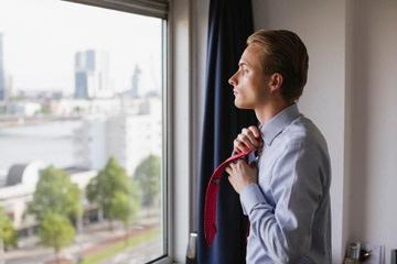Een student kijkt uit het raam en strikt zijn stropdas.
