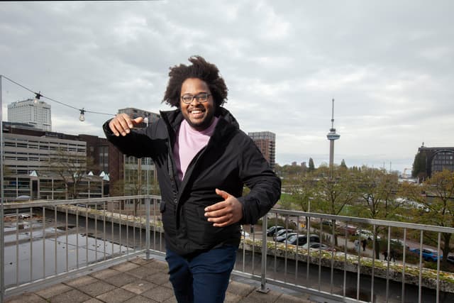 Foto van studentbeheerder Akili op het dak van de GEB-toren, met de Euromast op de achtergrond