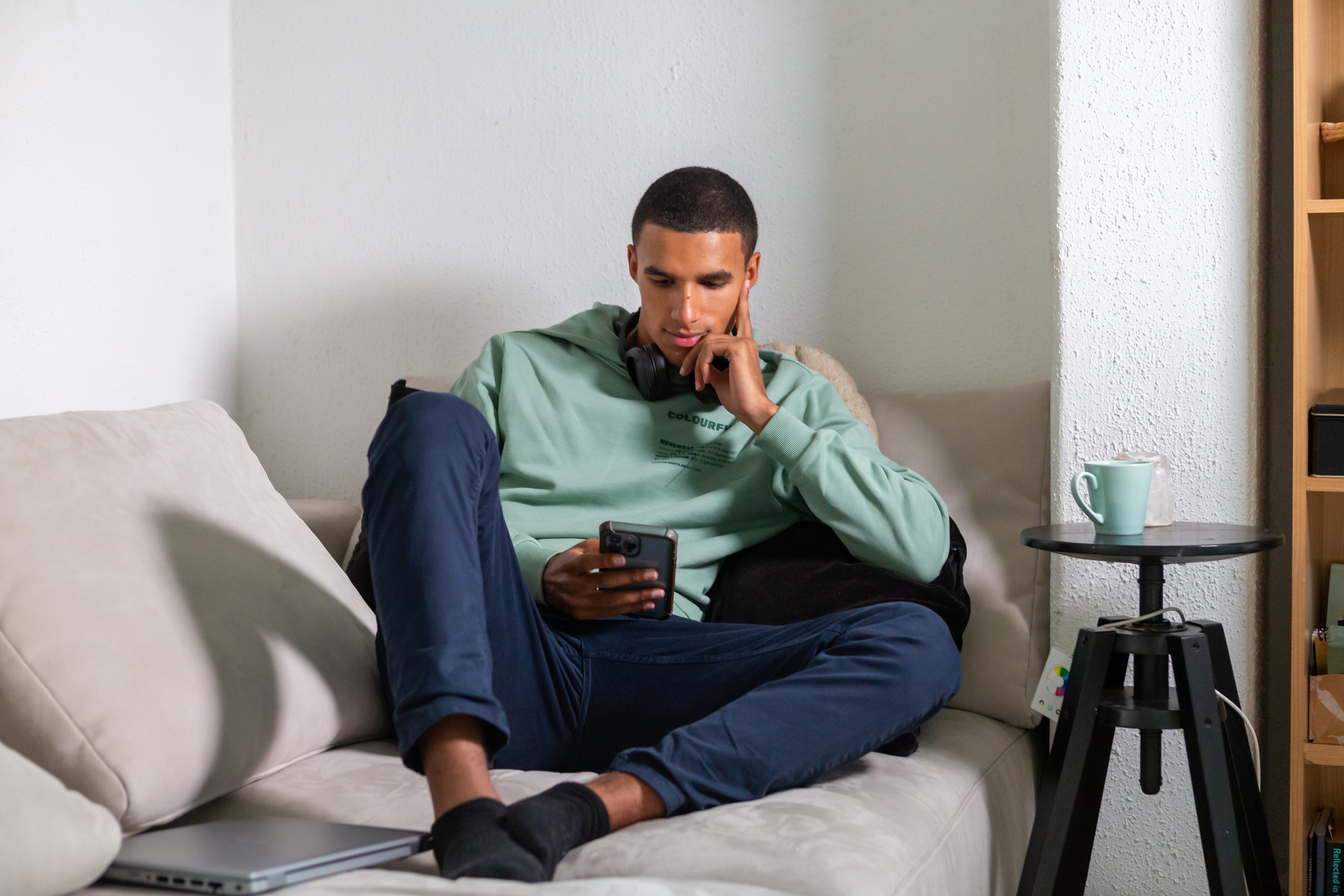 Een man zit met serieuze blik op de bank met een mobiele telefoon in zijn hand