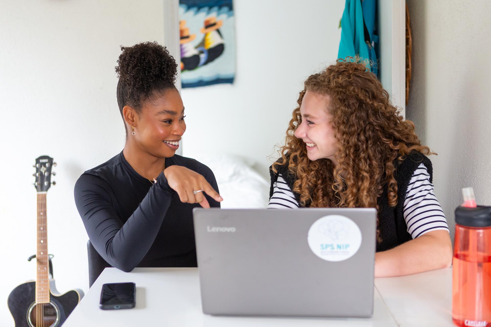 Twee dames die samen lachend achter een laptop zitten