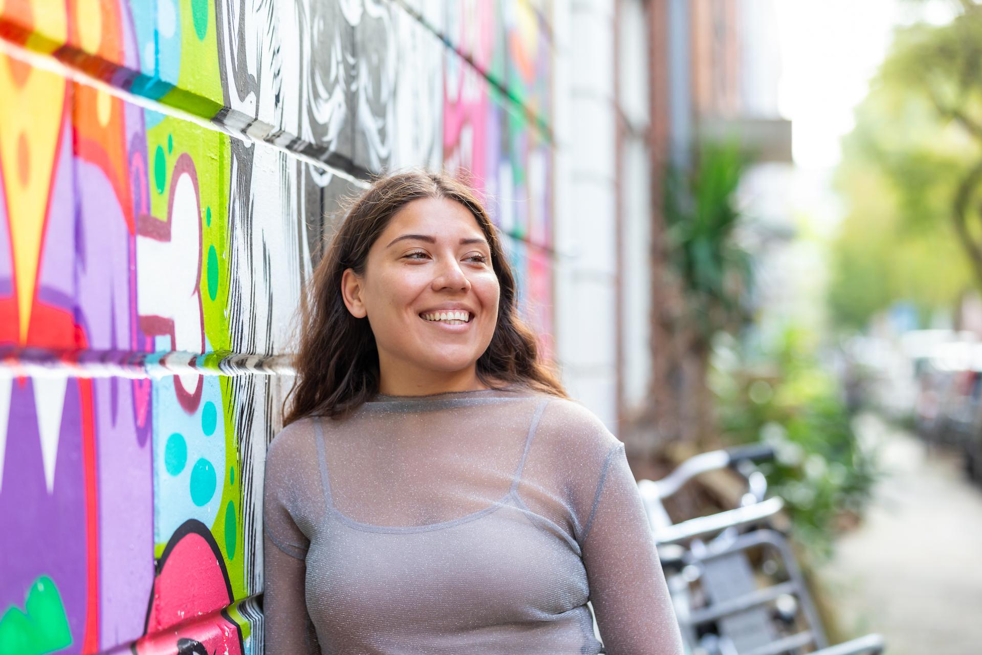 Lachende vrouw staat voor een vrolijk gekleurde graffiti muur.