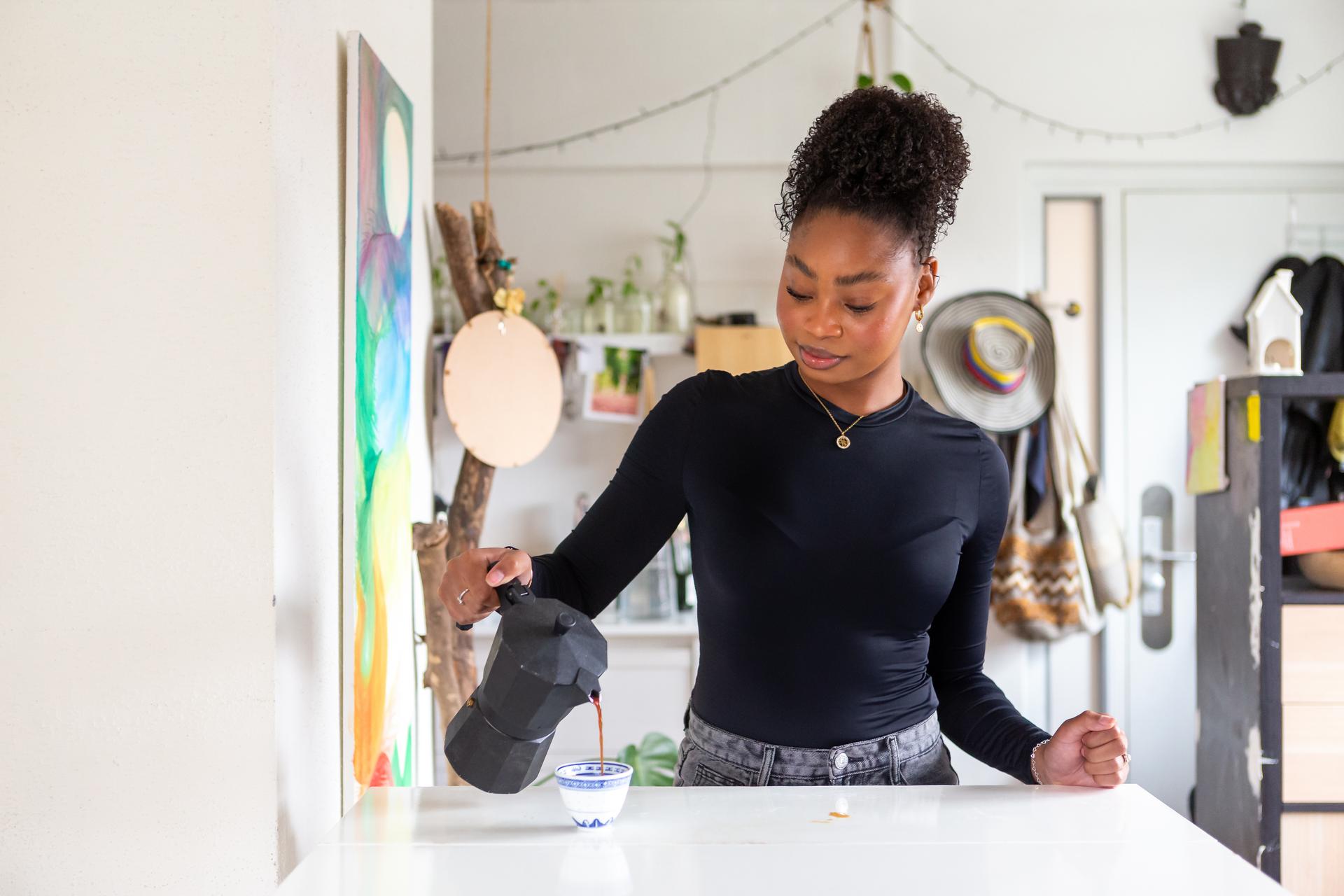 Vrouw staat alleen in haar keuken en schenkt een kop koffie in.
