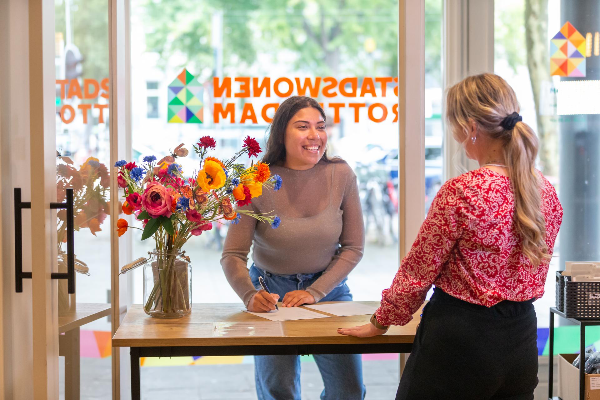 Lachende vrouw die handtekening zet bij de balie van het Stadswonen kantoor