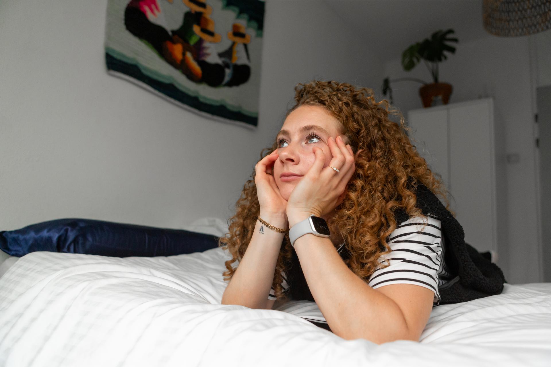 Vrouw ligt op haar buik en steunt haar hoofd op haar handen. Ze is niet blij.