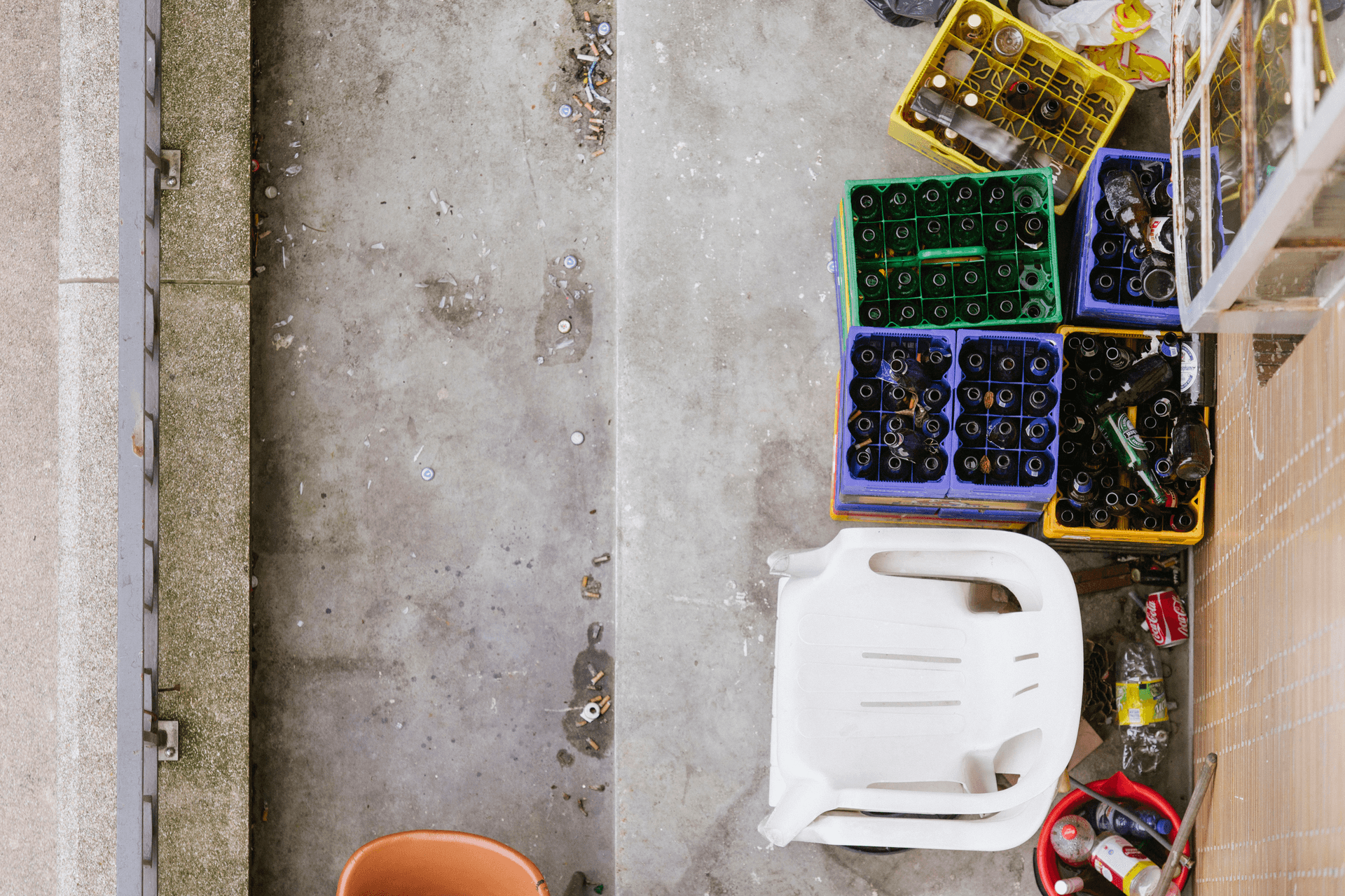 Een balkon met een tuinstoel en lege bierkratjes.