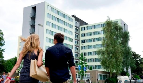 Een vrouw en man lopen buiten, op de achtergrond staat de studentenflat Alexander.