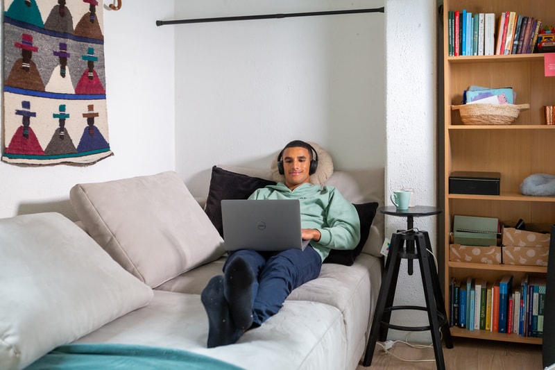 Student ligt op de bank met zijn laptop op schoot