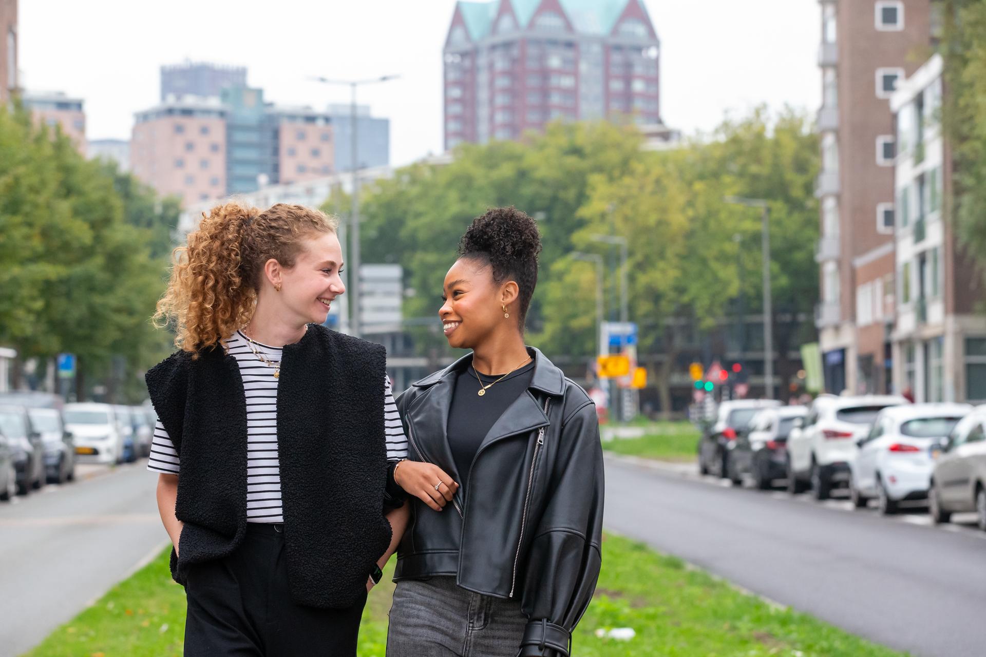 Twee vrouwen die lachend naar elkaar kijken terwijl ze over straat lopen
