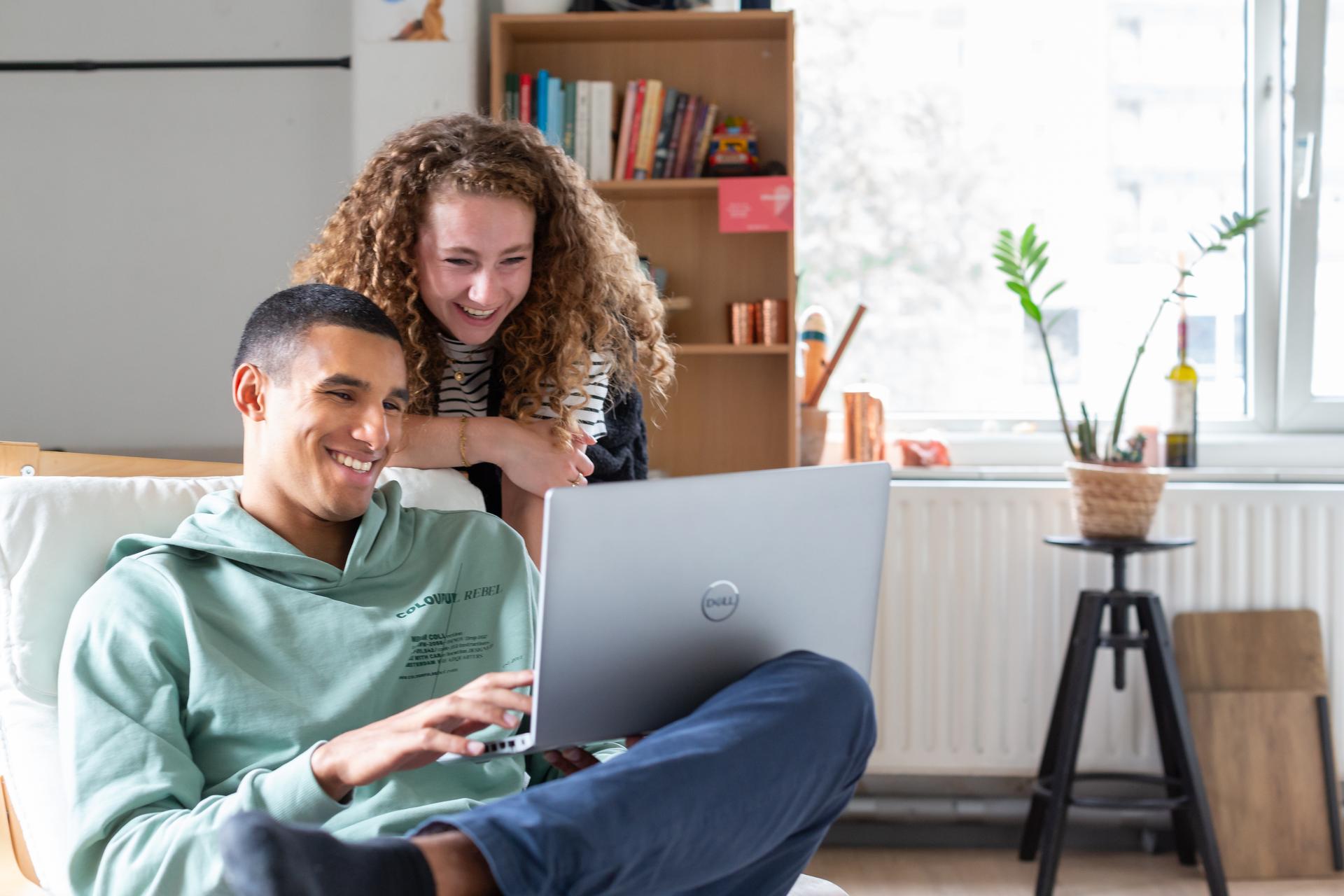 Een man en vrouw kijken samen lachend naar een laptop