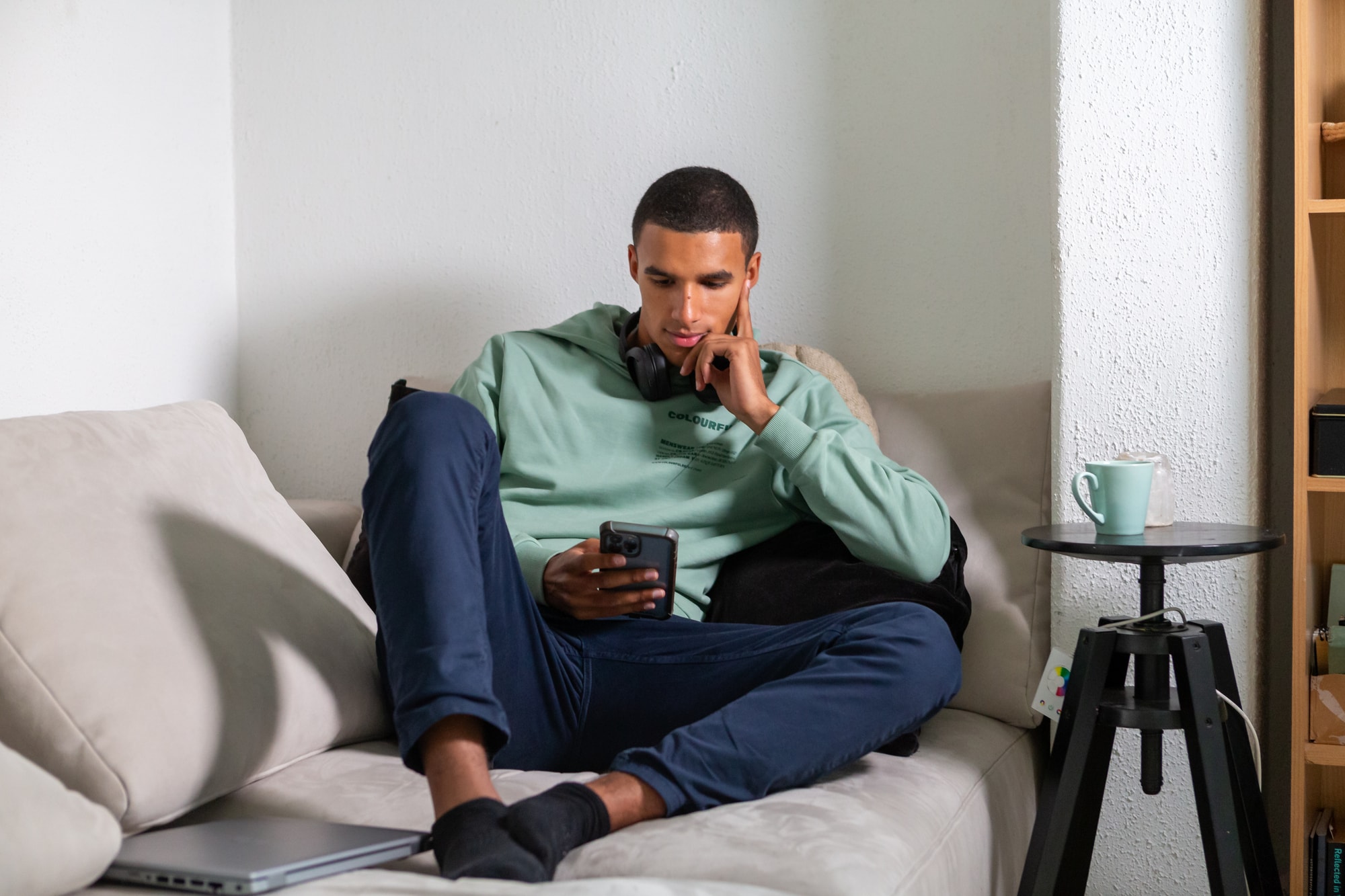 Een man zit met serieuze blik op de bank met een mobiele telefoon in zijn hand