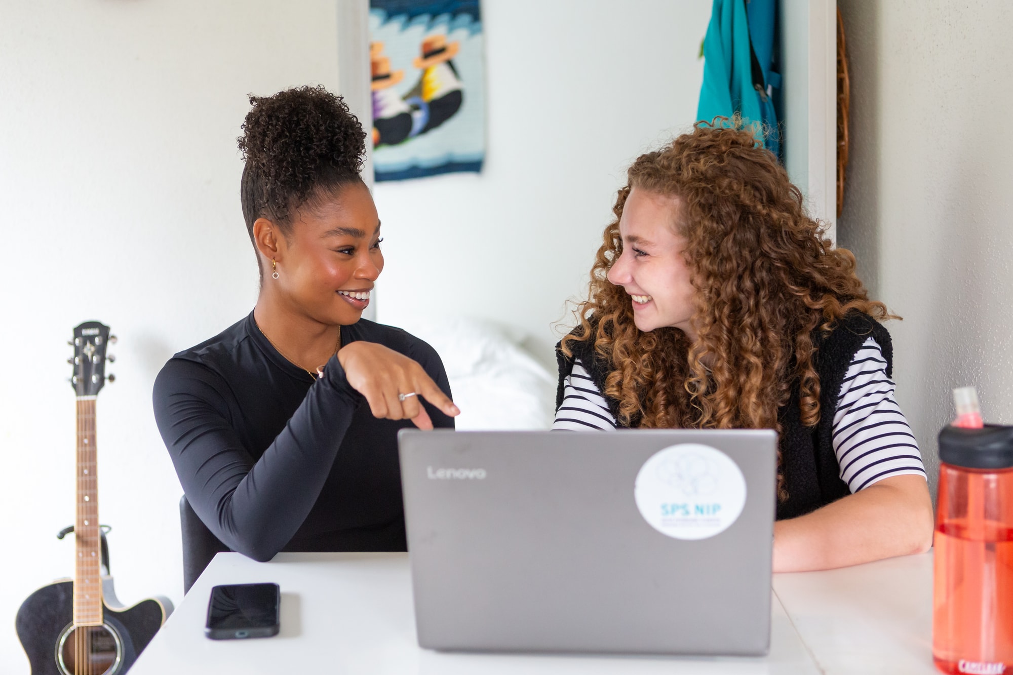 Twee dames die samen lachend achter een laptop zitten