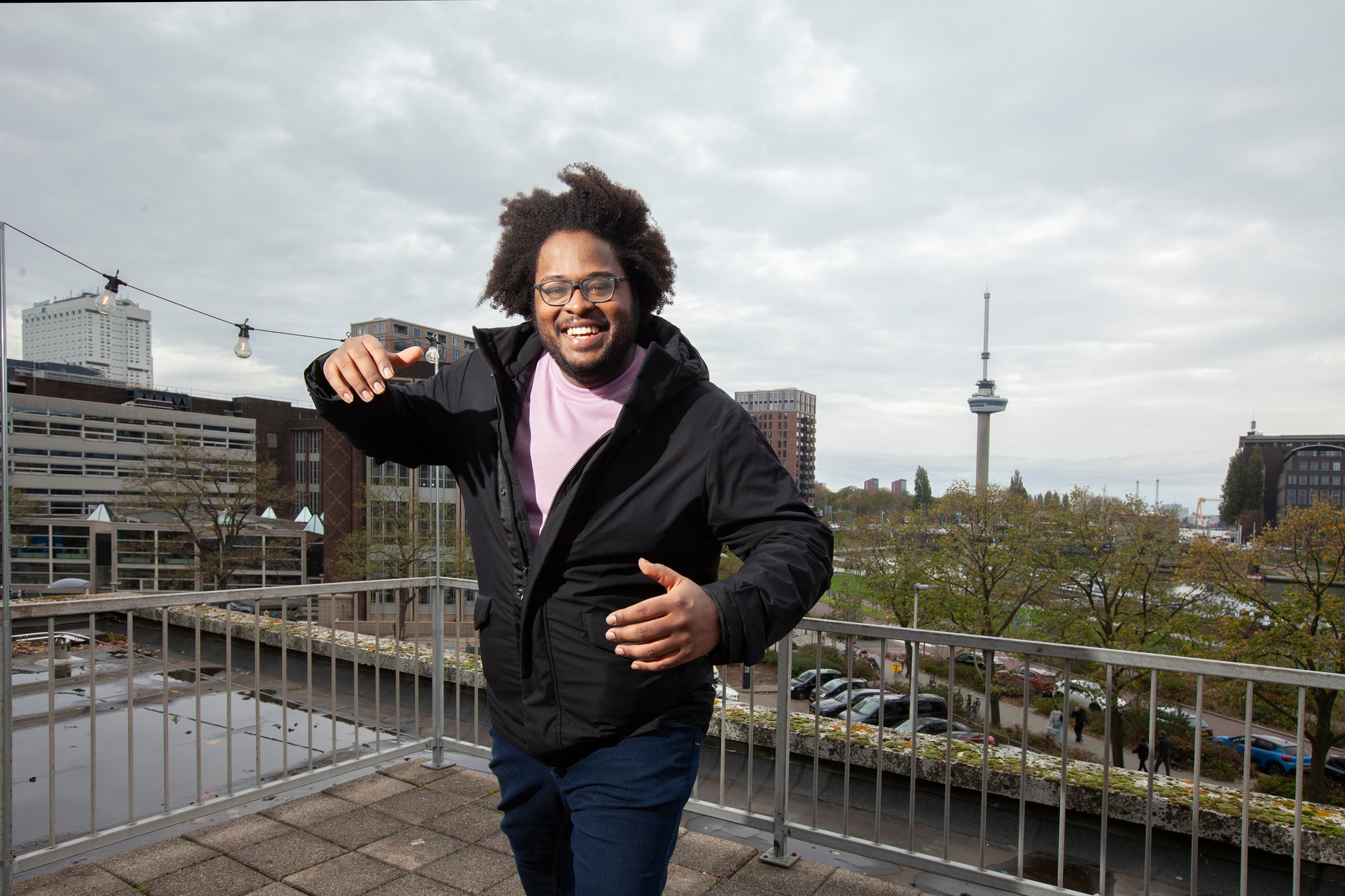 Foto van studentbeheerder Akili op het dak van de GEB-toren, met de Euromast op de achtergrond