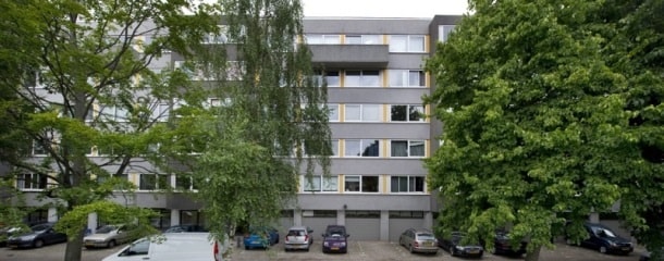 Foto van grijs gebouw met ramen. Er staan twee bomen voor.